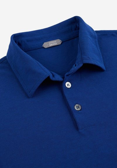 Polo shirt bleu marine en coton lisse avec un col pointe, présentant une patte de boutonnage à deux boutons et une étiquette d'entretien à l'intérieur du col.