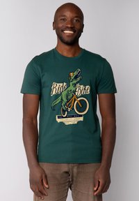 Grünes Baumwoll-T-Shirt mit einem Grafikdesign eines Dinosauriers, der Fahrrad fährt, und Text. Kurze Ärmel, Rundhalsausschnitt und lässige Passform.