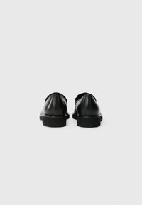 Chaussures en cuir noir avec une finition lisse, bout rond, talon bas et des détails cousus à l'arrière. Présente un design élégant et minimaliste.
