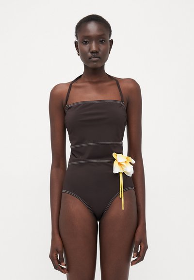 Costume da bagno marrone con spalline regolabili a spaghetti, cuciture bianche a contrasto e un fiore decorativo giallo con nastro in vita.
