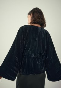 Black velvet kimono-style jacket with wide sleeves, featuring a smooth texture and subtle vertical stripes in the fabric.