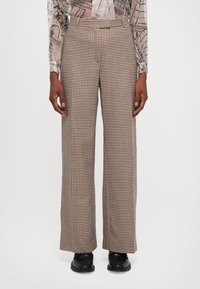 Wijde broek met een bruin-witte houndstoothprint, met een zachte textuur en een op maat gemaakte tailleband. Zwarte schoenen eronder gedragen.