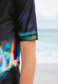 Kurzarm-Rashguard in Schwarz und Blau mit abstrakten Mehrfarbenmustern. Verfügt über eine verstärkte Naht am Ärmelabschluss für zusätzliche Strapazierfähigkeit.