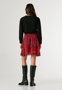 Musta neulepaita, jossa on teksturoitu kangas, yhdistettynä punakirjokuvioiseen hameeseen ja mustiin polvimittaisiin saappaisiin. Hameessa on joustava vyötärö.