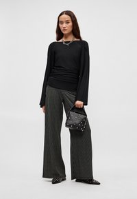 Must pikkade varrukatega topp, millel on kogutud detailid, sobitatud laiade must-valgete triibuliste pükstega. Kaunistatud naeltega musta käekotiga.