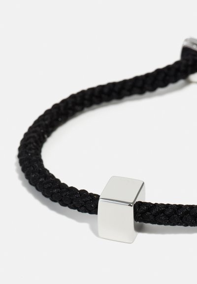 Bracelet tressé noir avec un fermoir rectangulaire en métal argenté, présentant une texture lisse et un design minimaliste.