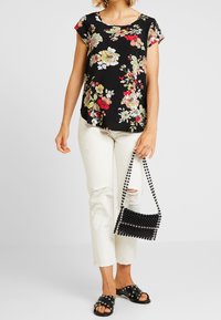 Svart blommig topp med korta ärmar, krämfärgade slitna jeans, svarta nitar sandaler och en liten svart pärlhandväska.