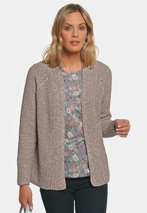 Gebreide cardigan in licht taupe met een textuursteekpatroon, open voorkant en geribbelde manchetten, gedragen over een top met bloemenprint.