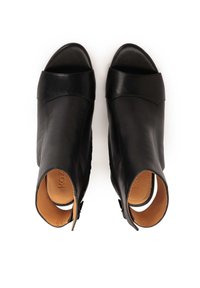 Sandales à talons en cuir noir avec un bout ouvert, un design structuré et des découpes sur les côtés, présentant une finition lisse et des accents minimalistes.