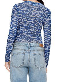 Långärmad topp i blå och grå abstrakt mönster, tillverkad av lättviktsmaterial, kombinerad med ljusblå denimjeans som har bakfickor och en läderetikett.