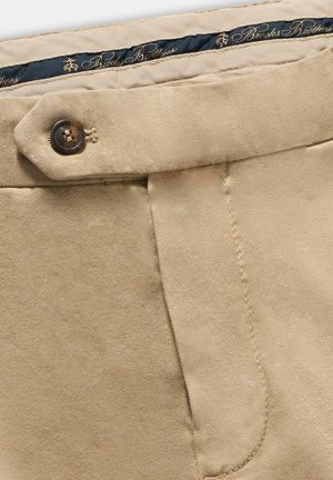Beige canvas broek met een gladde textuur, voorzien van een knoopsluiting, schuine zakken en een navy binnenband met gouden branding.
