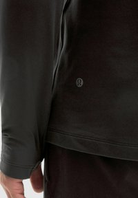 Fekete, hosszú ujjú felső, puha anyagból készült, testhez simuló fazonnal, a hemmentén varrási részletekkel és egy diszkrét logóval az alján.