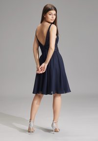 Abito blu navy con profondo scollo a V sul retro, corpino decorato e gonna di chiffon fluida. Abbinato a sandali con tacco argento.