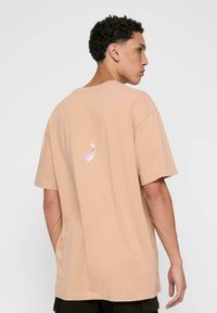 Lys fersken oversized t-skjorte, laget av bomull, med rund hals, korte ermer, med et subtilt grafisk design på ryggen.