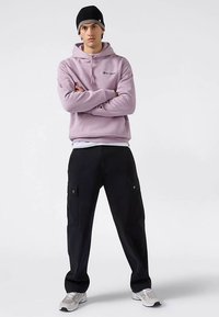 Svetlofialová mikina s kapucňou s vyšívaným logom, kombinovaná s čiernymi cargo nohavicami s bočnými vreckami a striebornými prvkami.