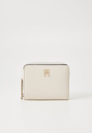 Portafoglio in pelle beige con una texture liscia, caratterizzato da un accento del logo dorato e una chiusura con zip lungo il bordo superiore. Design compatto e rettangolare.