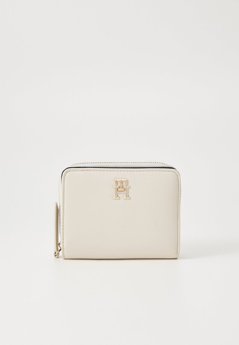 Portefeuille en cuir beige avec une texture lisse, présentant un accent logo doré et une fermeture éclair le long du bord supérieur. Design rectangulaire compact.