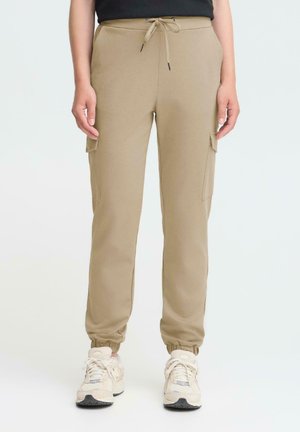 Beige Cargo-Hosen mit elastischen Bündchen, Seitentaschen und verstellbarem Kordelzugbund; kombiniert mit weißen Sneakern mit grauen Akzenten.