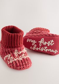 Czerwone dziergane buciki dla niemowląt z mankietami z prążkowanej dzianiny. Na boku haftowany biały napis „moje pierwsze Święta”. Miękki, teksturowany wzór.