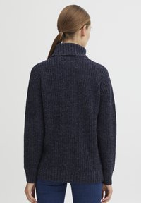 Navy knitted sweater featuring a high collar, textured fabric, ribbed cuffs, and a slightly loose fit, suitable for casual wear.