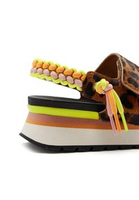 Sandale à imprimé léopard avec une sangle tressée multicolore, une plateforme épaisse et une semelle superposée avec des accents noirs, orange, rose et jaune.