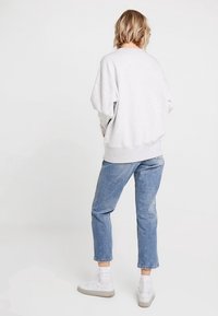 Světlounce šedá mikina s pokleslými rameny, žebrovanými manžetami a lemem. Kombinována s modrými džínami a bílými teniskami, pohled zezadu.