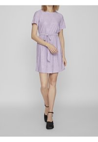 Short lavender dress with short sleeves, belted waist, and eyelet detail throughout. Worn with black ankle-strap shoes.