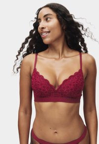 Red lace bralette featuring a V-neck design, delicate floral patterns, adjustable straps, and a textured band for support.