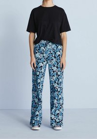 Černé tričko s krátkým rukávem spárované s květinovými, širokými kalhotami modro-bílé barvy na černém pozadí. Bílé tenisky dotvářejí celý outfit.