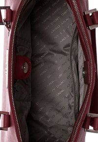 Inuti en vinröd handväska med en slät läderyta, som visar ett mönstrat grått foder och en dragkedjeficka med knappstängning.