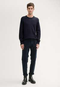 Maglione lavorato a maglia blu navy, con polsini a coste, abbinato a pantaloni in velluto a coste scuri e stivaletti neri alla caviglia. Design semplice con una vestibilità comoda.