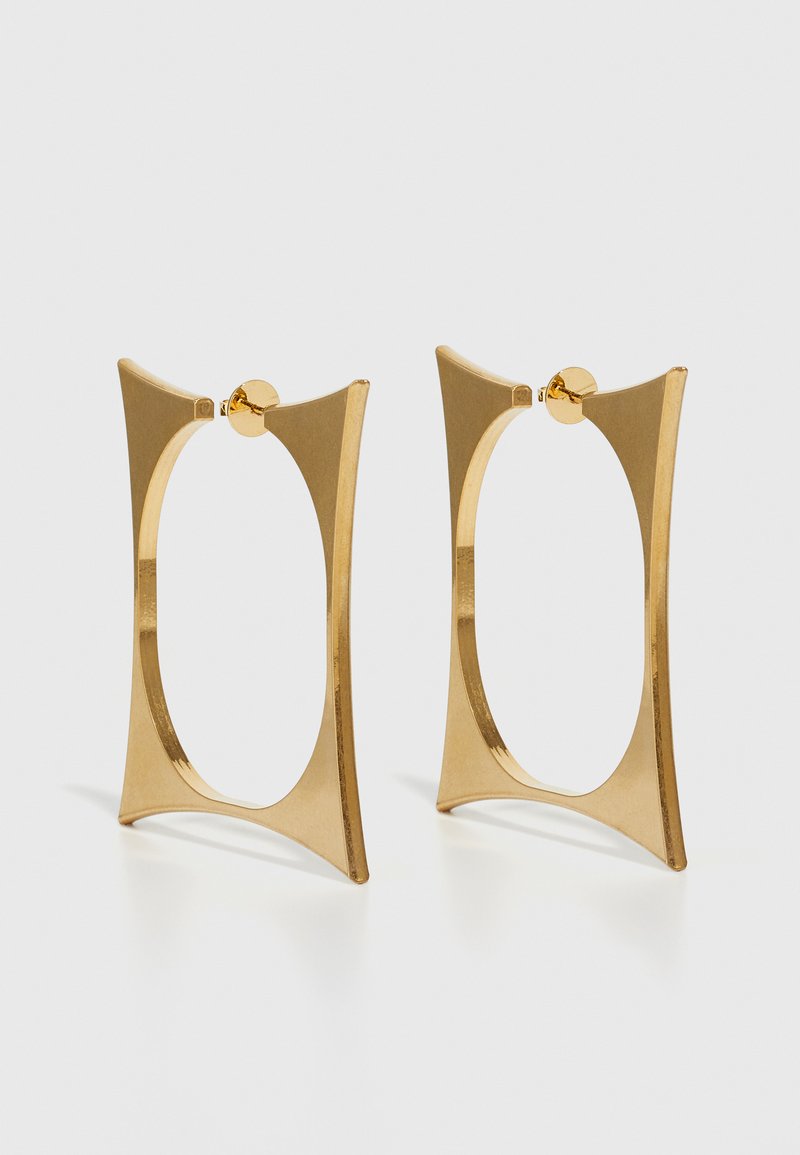 Aukso tono auskarai žiedų pavidalu su geometriniu dizainu, kuriame yra kvadrato forma ir kreivi išpjovimai. Lygi tekstūra su blizgiu paviršiumi.