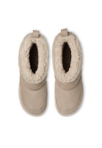 Une paire de bottes de cheville beiges avec une doublure en shearling douce et duveteuse et des languettes de tirage, vue de dessus sur un fond blanc.