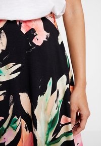 Jupe imprimée florale avec un fond noir, présentant de grands motifs de feuilles vertes et roses. Fabriquée en tissu doux ; design mi-long.