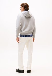 Γκρι φούτερ με κουκούλα και κορδόνι, με ριμπ navy λεπτομέρεια στη μέση, συνδυασμένο με λευκό παντελόνι και μαύρα παπούτσια. Απλός και καθημερινός σχεδιασμός.