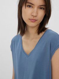 Modra majica z V-izrezom in kratkimi rokavi, izdelana iz mehkih materialov, z gladko teksturo in sproščenim krojem, ki dopolnjuje nevtralen ozadje.