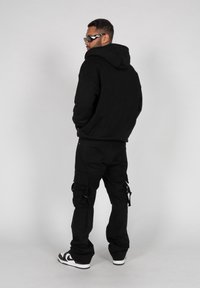 Zwarte hoodie met een kangoeroezak, gecombineerd met zwarte cargobroeken met zijzakken en witte sneakers.