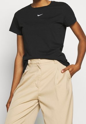 Zwart T-shirt met korte mouwen en een wit Nike-logo op de borst, gecombineerd met beige broek met hoge taille, met een losse pasvorm.
