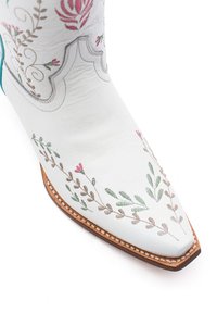 Stivale da cowboy in pelle bianca con ricamo floreale in rosa e verde, punta appuntita e cuciture di accento marrone lungo la suola.