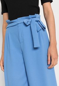 Ljusblå vida byxor i mjukt tyg, med en knuten sash i midjan och framfickor, samt sidofickor.
