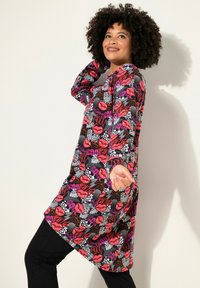 Tunika colorata con labbra rosse e motivi testuali su uno sfondo nero; tessuto morbido, maniche lunghe e vestibilità rilassata, abbinata a pantaloni neri.