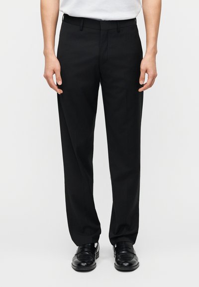 Μαύρο tailored παντελόνι με ίσια εφαρμογή, κατασκευασμένο από απαλό ύφασμα. Διαθέτει θηλιές για ζώνη και τσέπες, συνδυασμένο με μαύρα επίσημα παπούτσια.