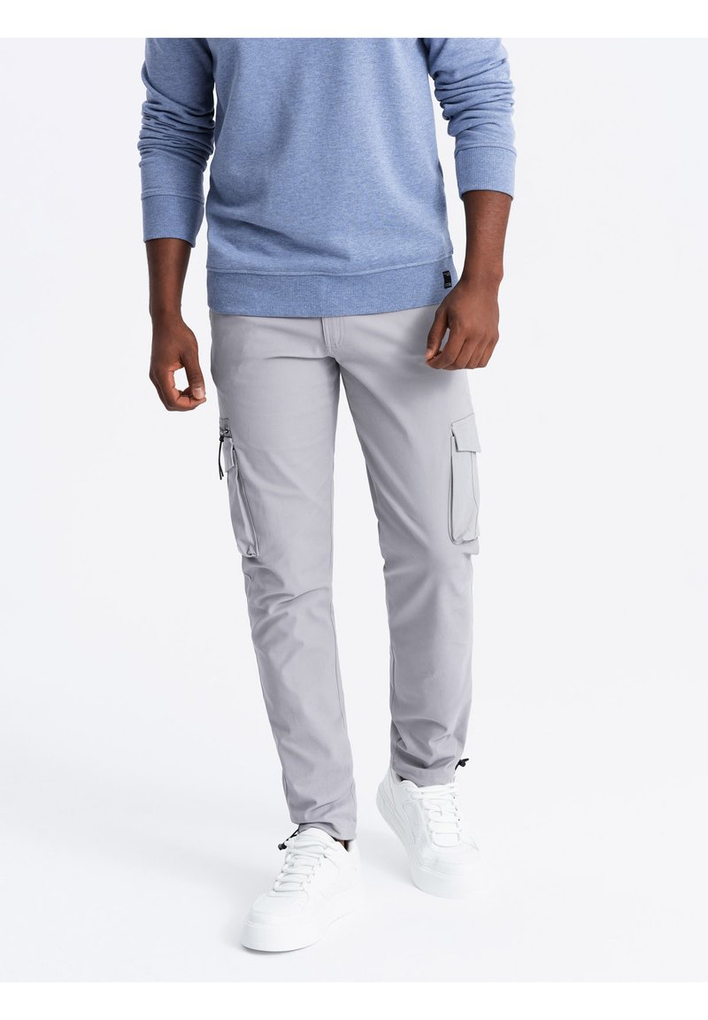 Lichtgrijze cargobroek met twee zijzakken. Gemaakt van duurzaam materiaal, met een tapered fit en gestikte details. Gedragen met witte sneakers.