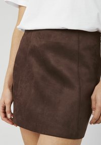 Mini-jupe en daim marron avec une texture lisse, un design ajusté et des lignes épurées, présentant un léger éclat et sans garniture visible.