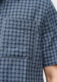 Chemise à manches courtes à carreaux bleu et blanc avec une poche poitrine comportant une petite étiquette noire Hollister.