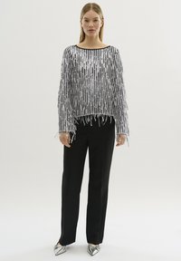 Top con frange argentate, vestibilità ampia, maniche lunghe e pantaloni neri. Texture interessante grazie ai dettagli in frange verticali; design elegante, abbinato a scarpe metalliche.