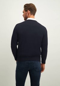 Marineblauwe gebreide trui met een ronde halslijn, geribbelde boorden en zoom, gecombineerd met donkere spijkerbroek met achterzakken, zonder zichtbare patronen.
