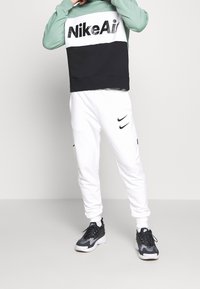 Nike Air sweatshirt har en färgblockdesign i svart, vitt och grönt. Tillsammans med vita joggerbyxor, som båda inkluderar logodetaljer. Svarta sneakers fulländar looken.