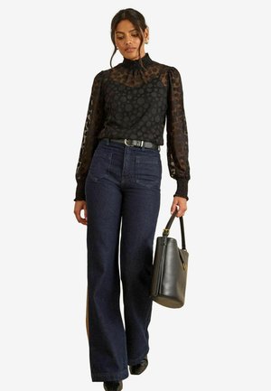 Black polka dot blouse with sheer texture, high neck, and puffed sleeves paired with dark wide-leg jeans and a black handbag.