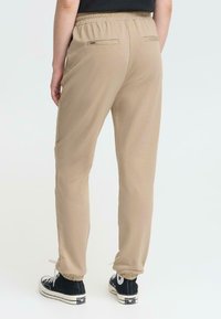 Beige trainingsbroek met elastische tailleband, achterzakken, taps toelopende pijpen en trekkoorddetail, gecombineerd met zwarte high-top sneakers.